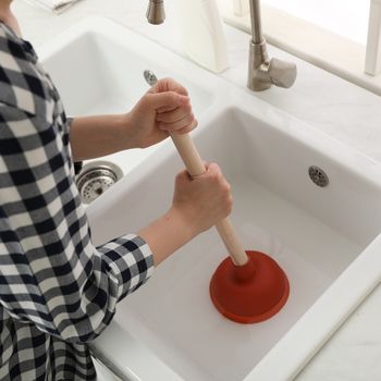 woman using plunger to unclog sink drain