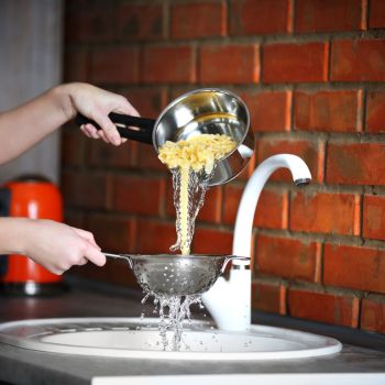 pouring water from boiled pasta over sink